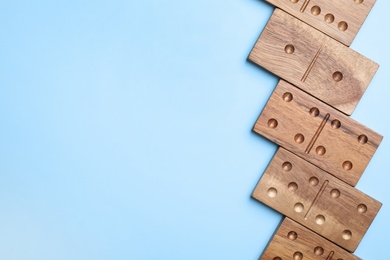 Wooden domino tiles on light blue background, flat lay. Space for text