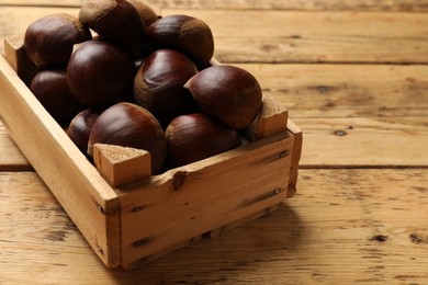 Sweet fresh edible chestnuts in crate on wooden table, closeup. Space for text