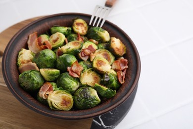 Photo of Delicious roasted Brussels sprouts and bacon in bowl on white table, closeup
