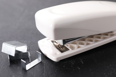 Photo of Beige stapler with staples on black textured table, closeup