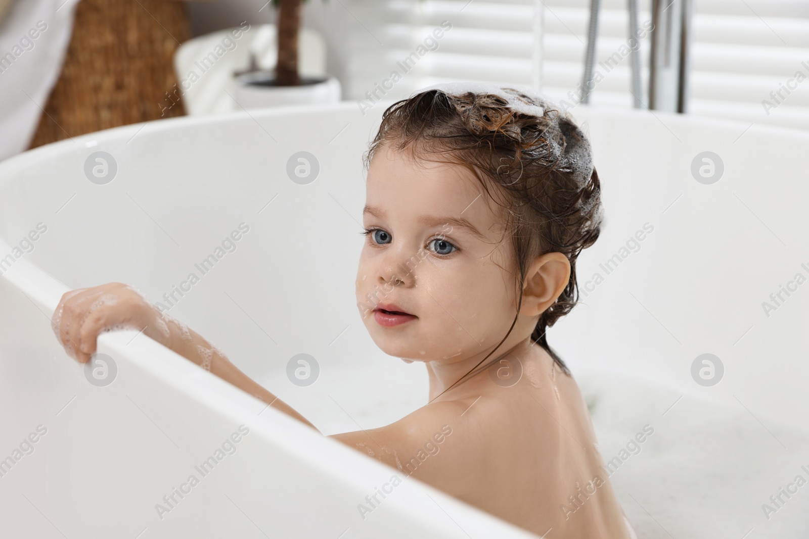 Photo of Cute little girl washing hair with shampoo in bathroom