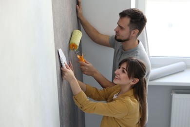 Photo of Couple hanging stylish gray wallpaper in room