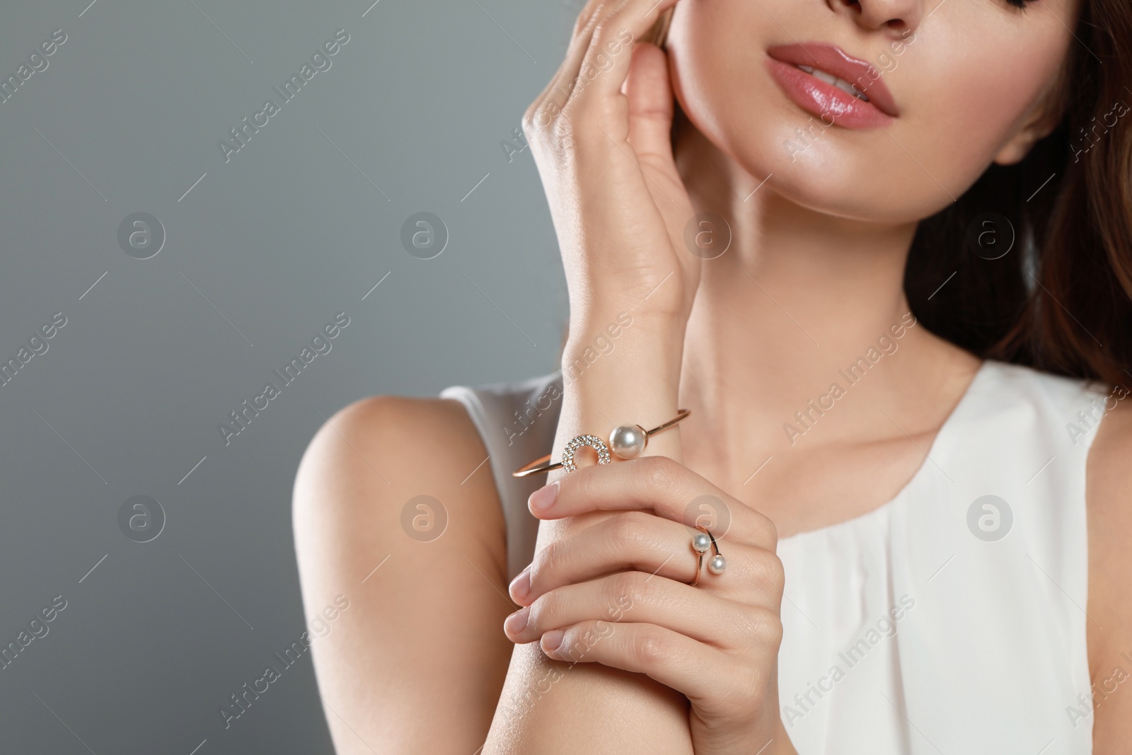 Photo of Young woman wearing elegant pearl jewelry on grey background, closeup. Space for text