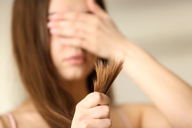 Photo of Emotional woman with damaged hair on blurred background, selective focus. Split ends