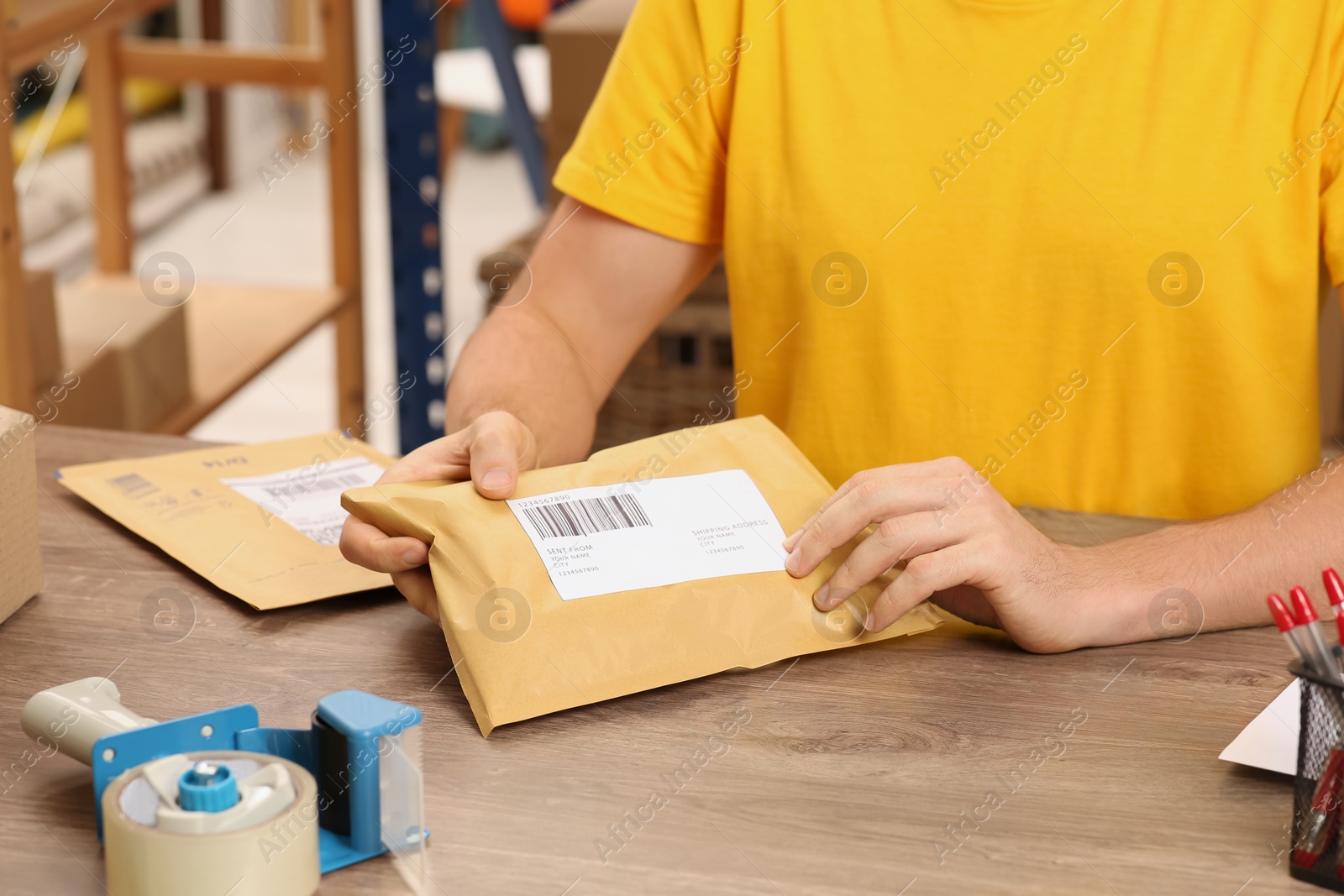 Photo of Post office worker sticking barcode on parcel at counter indoors, closeup