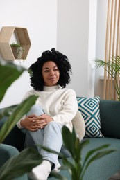 Relaxing atmosphere. Woman sitting on sofa near beautiful houseplants at home