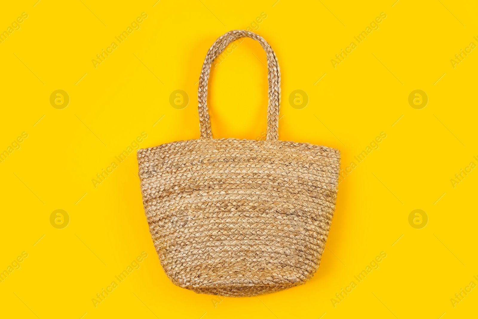 Photo of Stylish woman's straw bag on yellow background, top view