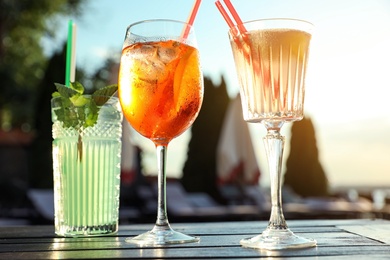 Photo of Glasses of fresh summer cocktails on table outdoors at sunset, low angle view