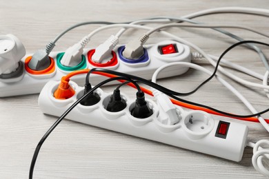 Photo of Power strip with extension cords on white wooden floor. Electrician's equipment