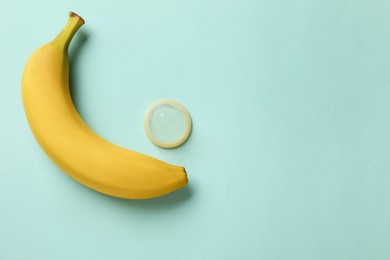 Photo of Banana and condom on turquoise background, flat lay with space for text. Safe sex concept