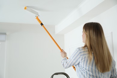 Photo of Young woman painting ceiling with white dye indoors, back view