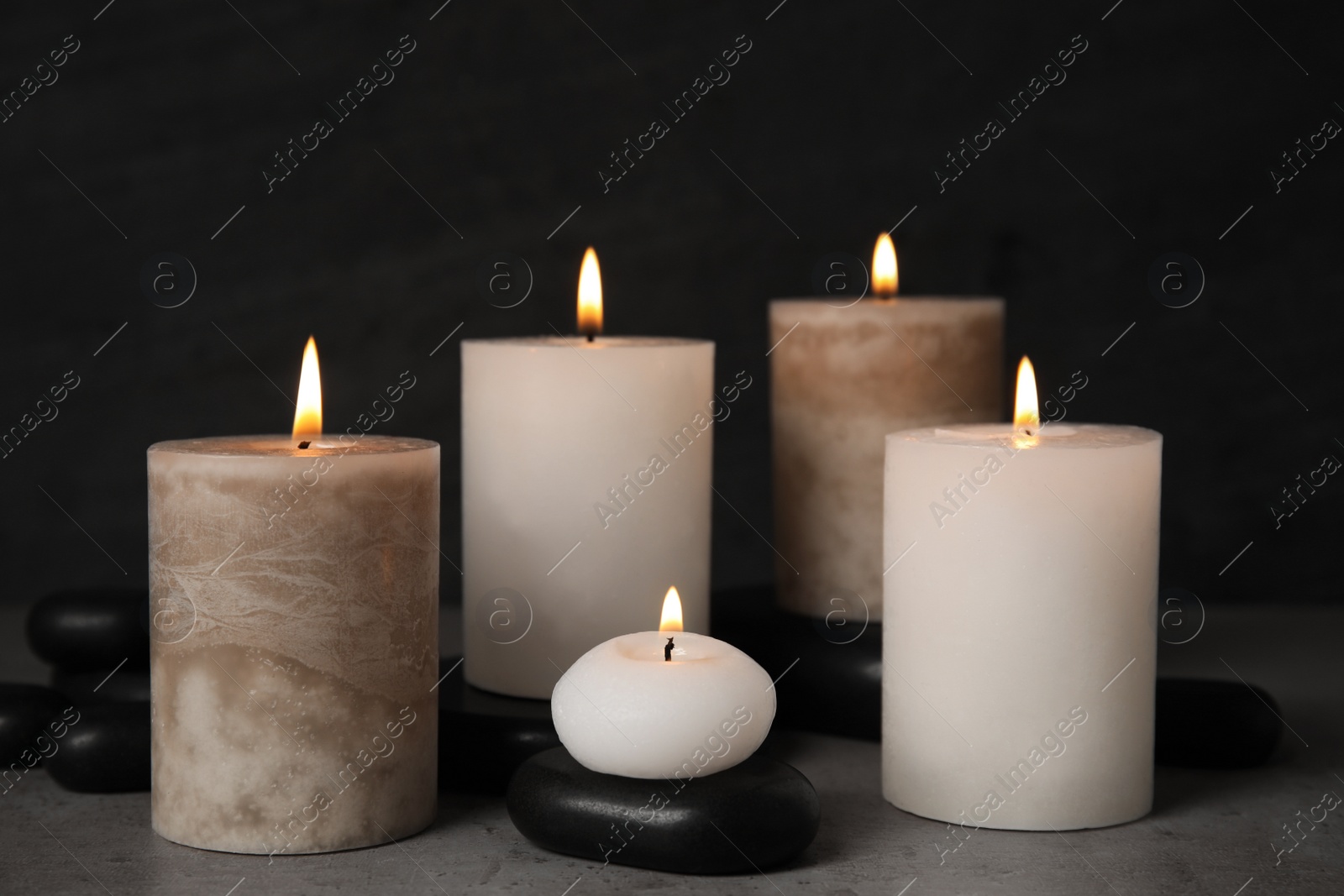 Photo of Burning candles and spa stones on grey table