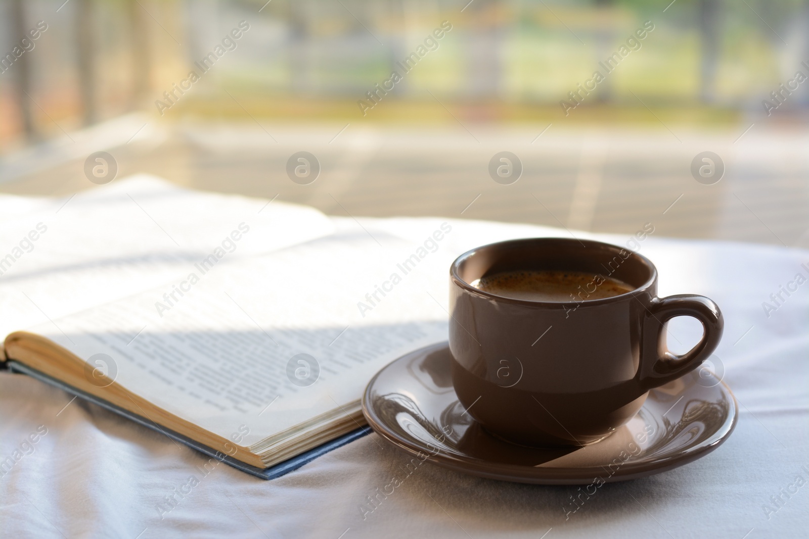 Photo of Aromatic morning coffee and open book on bed indoors