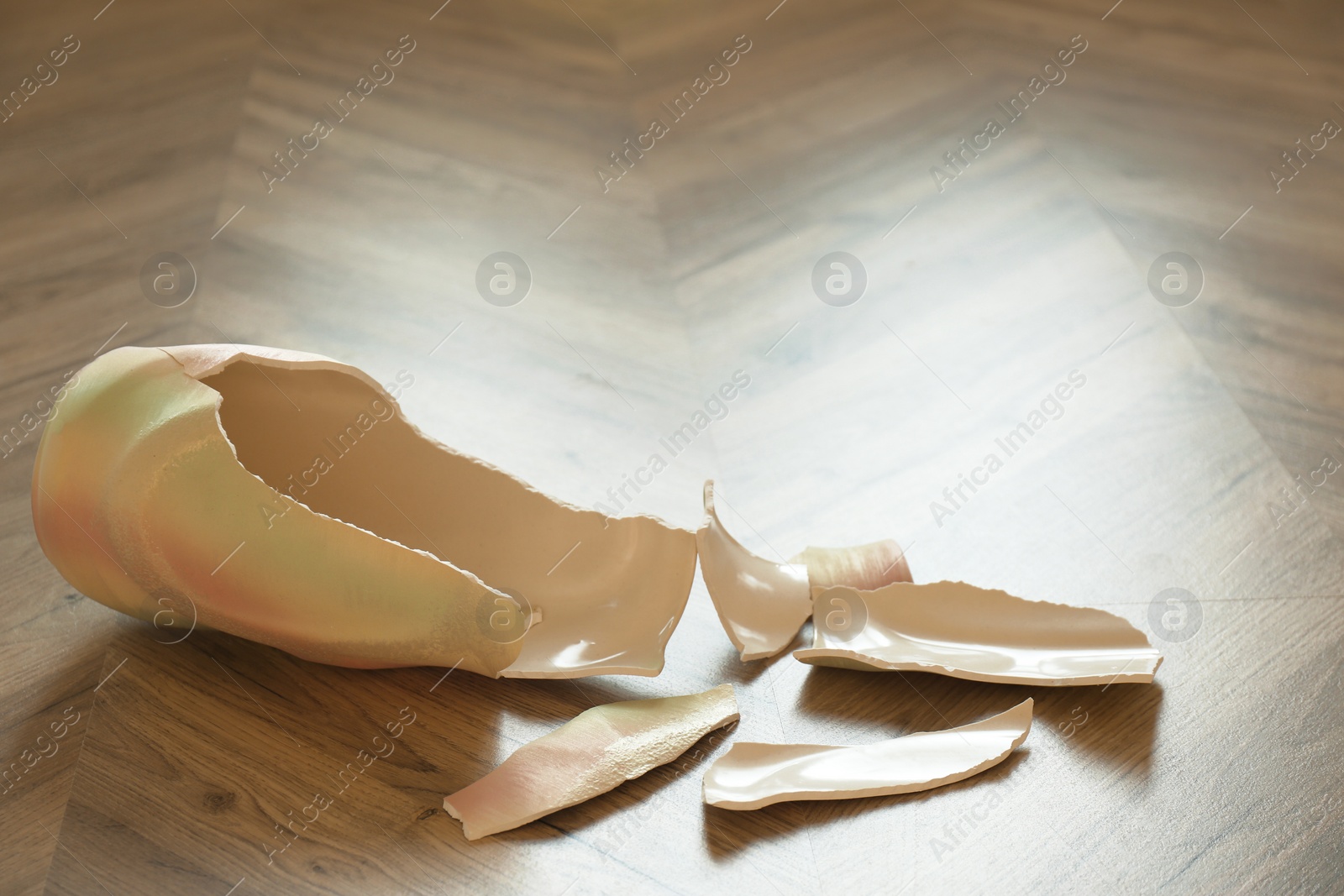 Photo of Broken bright ceramic vase on wooden floor. Space for text