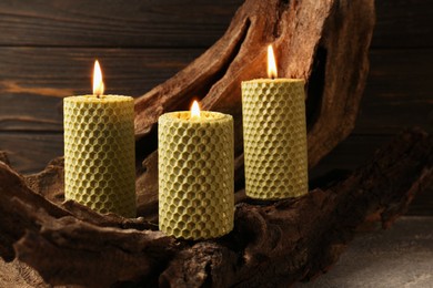 Photo of Beautiful burning beeswax candles on snag near wooden wall