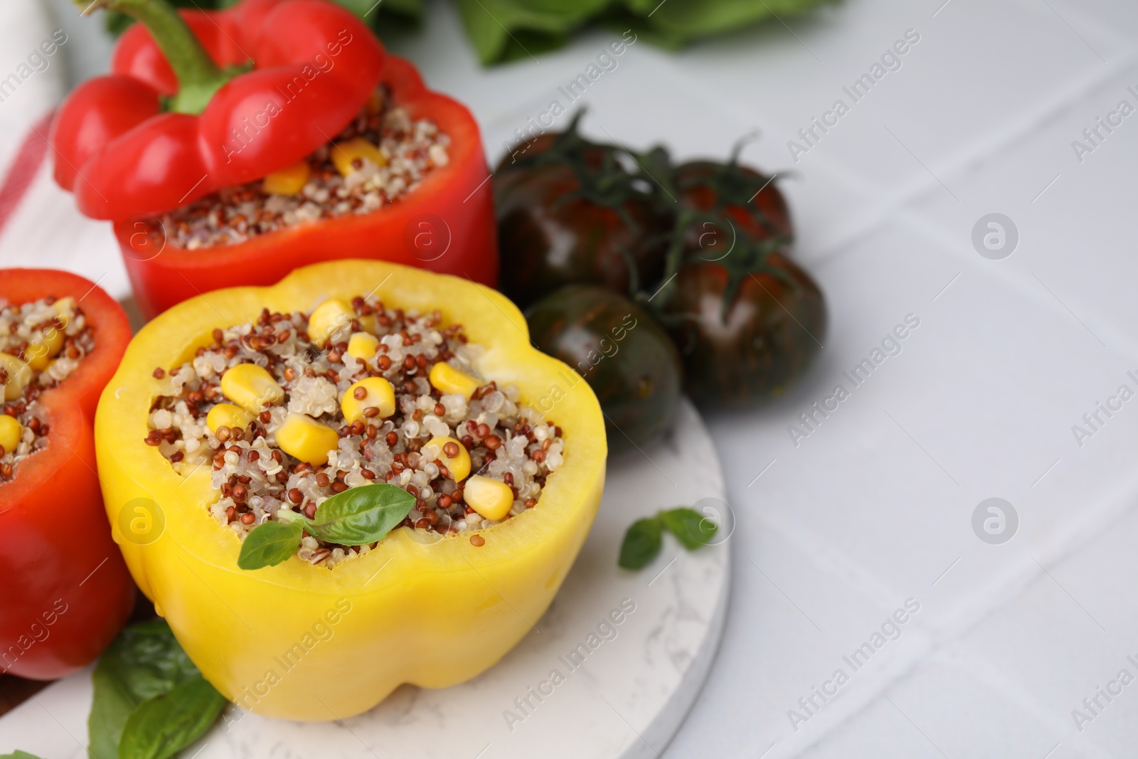 Photo of Quinoa stuffed bell peppers, basil and tomatoes on white tiled table, closeup. Space for text