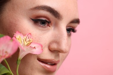 Beautiful woman with fake freckles and flowers on pink background, closeup. Space for text