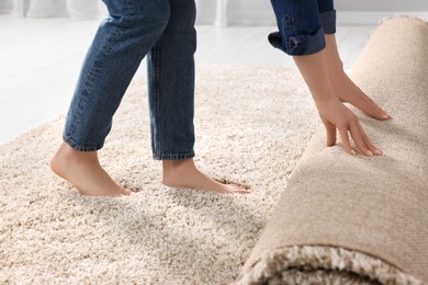Photo of Woman unrolling carpet on floor in room, closeup