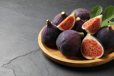 Plate with fresh ripe figs and green leaf on black table, closeup. Space for text