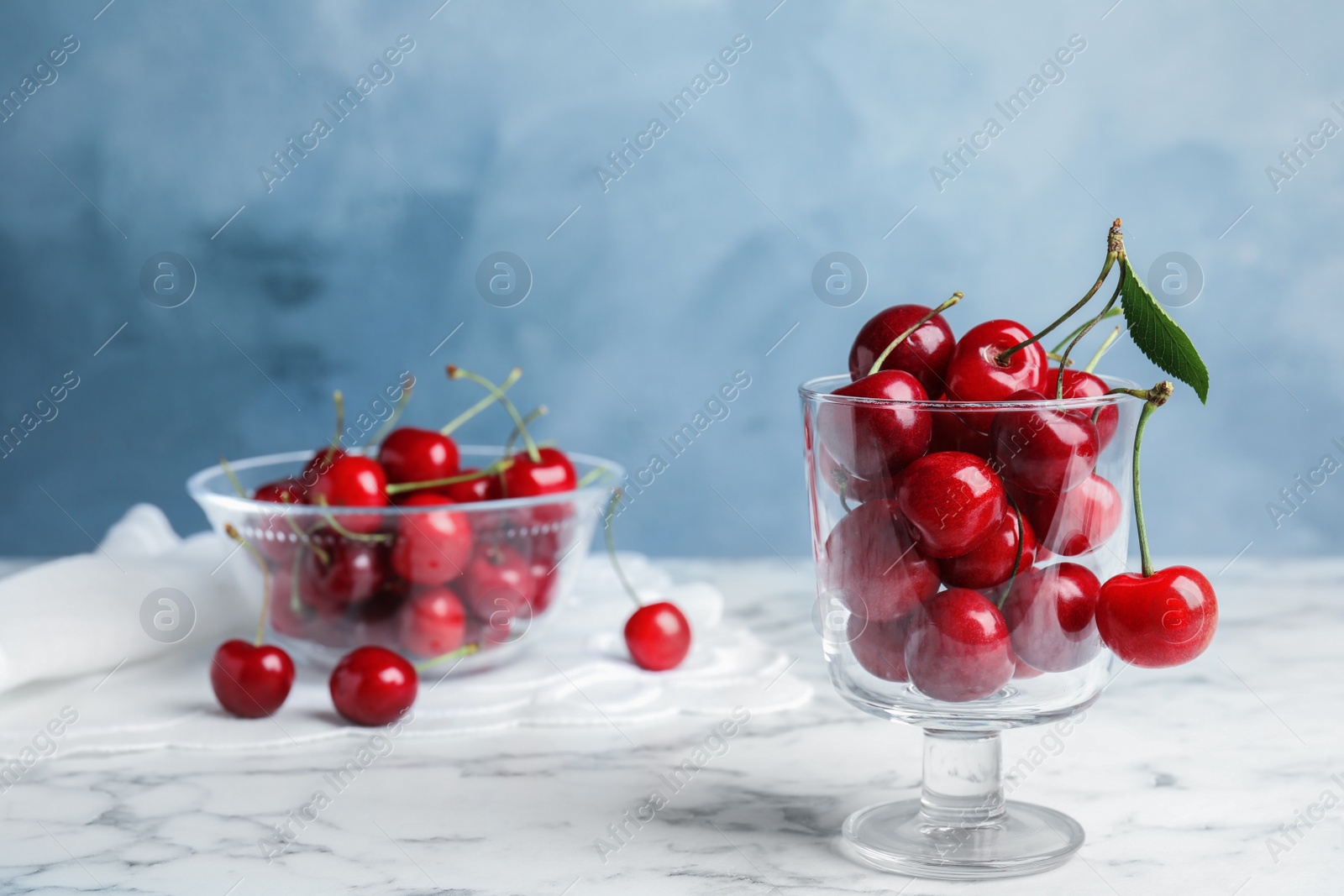 Photo of Glass dessert bowl with ripe sweet cherries on marble table. Space for text