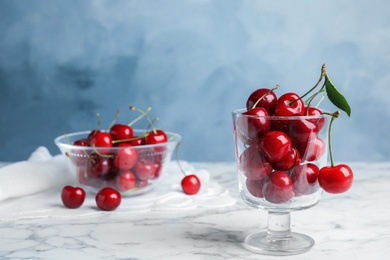 Glass dessert bowl with ripe sweet cherries on marble table. Space for text