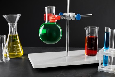 Photo of Retort stand and laboratory glassware with liquids on table against black background