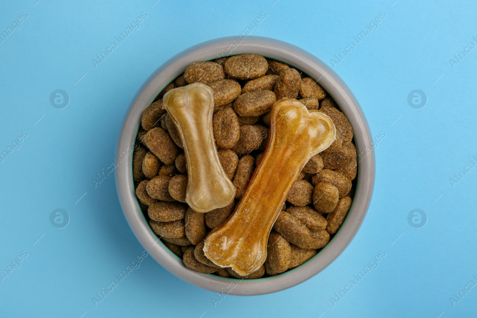 Photo of Dry dog food and treats (chew bones) on light blue background, top view