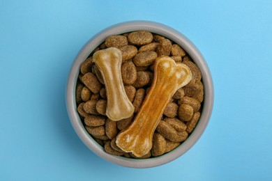 Photo of Dry dog food and treats (chew bones) on light blue background, top view