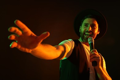 Photo of Handsome man with microphone singing in neon lights on dark background