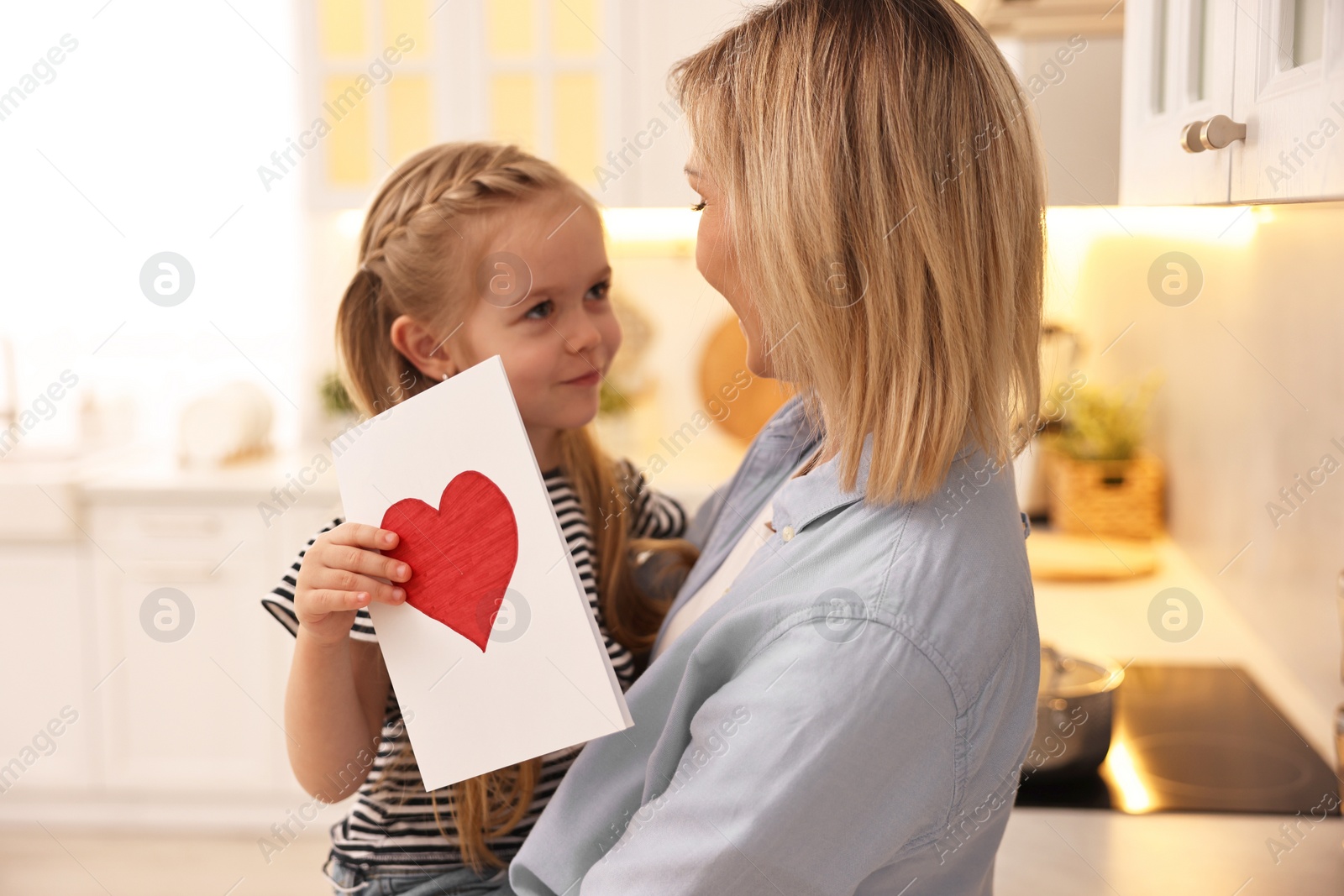 Photo of Little daughter congratulating her mom with greeting card in kitchen. Happy Mother's Day