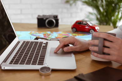 Woman using laptop to plan trip at wooden table, closeup