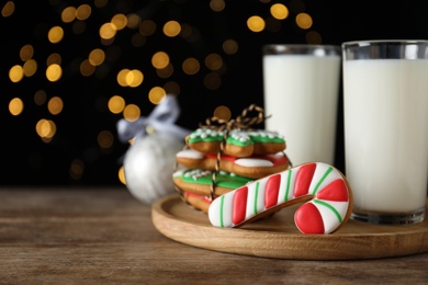 Tasty Christmas cookies and milk on wooden table against black background with blurred lights