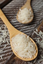 Photo of Raw basmati rice in spoon on wooden table, closeup