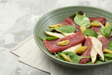 Photo of Delicious bresaola salad in bowl on light textured table, closeup. Space for text