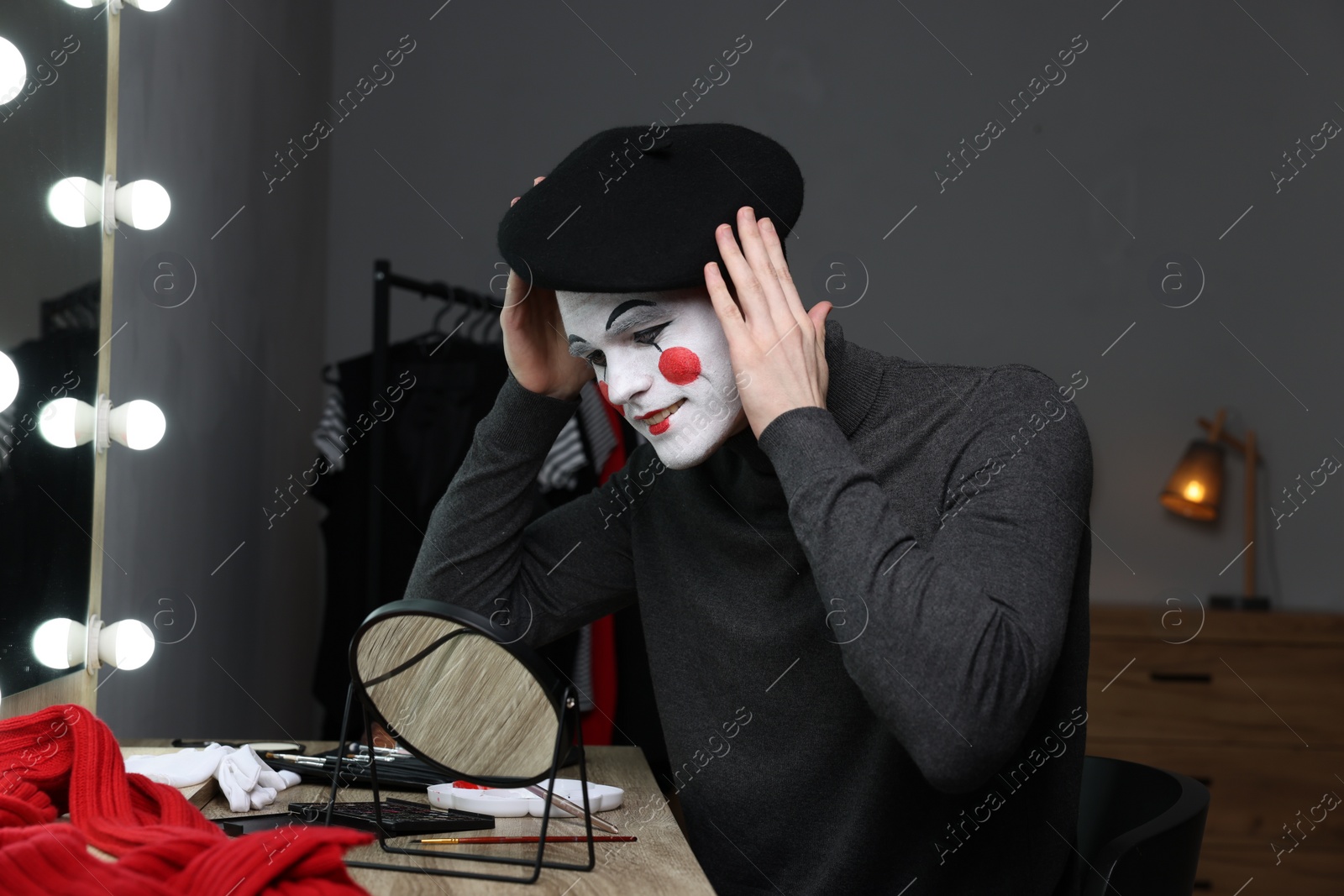 Photo of Mime artist putting on beret near mirror in dressing room