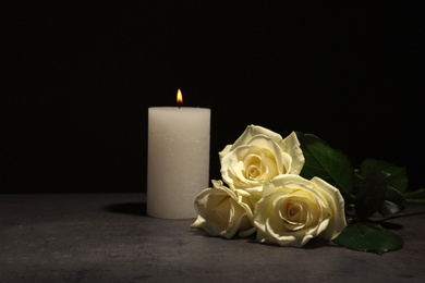 Beautiful white roses and candle on table against black background. Funeral symbol