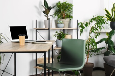 Photo of Beautiful workplace with laptop on wooden table, chair and houseplants in room