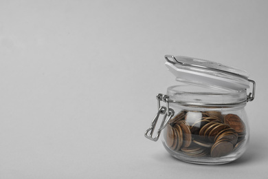 Photo of Glass jar with coins on light background, space for text