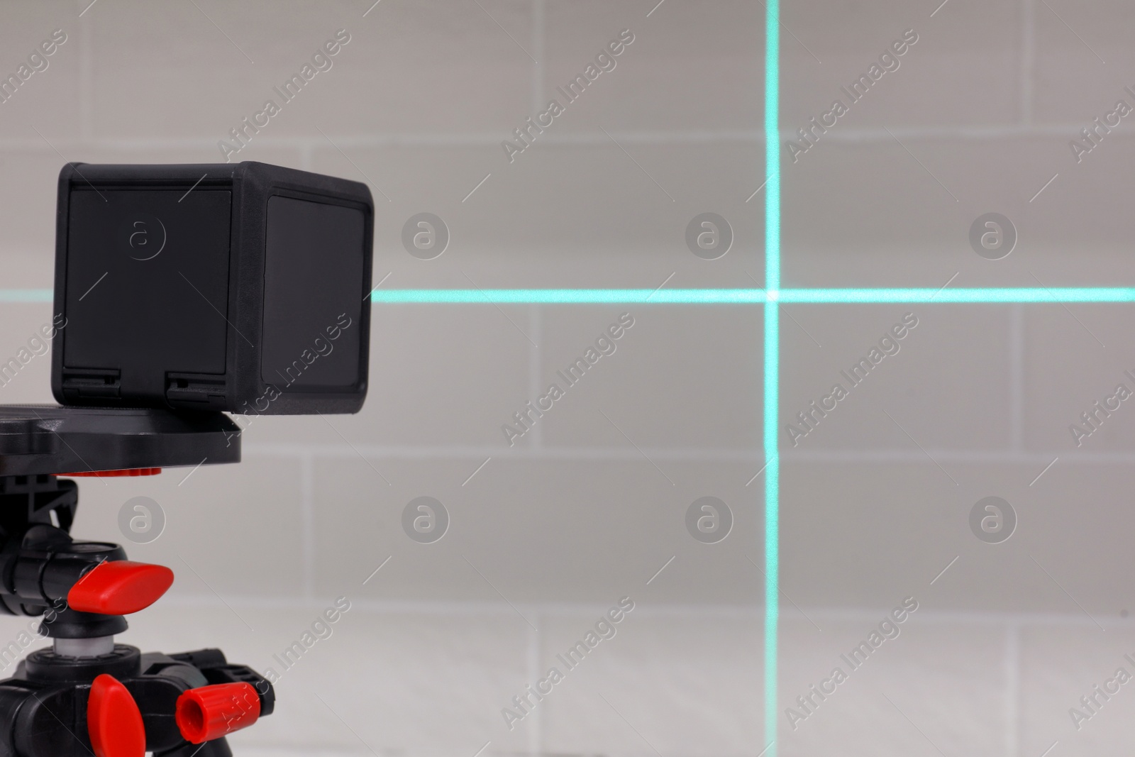 Photo of Cross line laser level on tripod in front of white brick wall