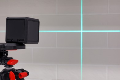 Photo of Cross line laser level on tripod in front of white brick wall