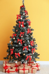 Beautiful Christmas tree with gifts near color wall. Celebration time