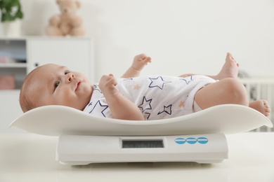 Photo of Cute little baby lying on scales in light room