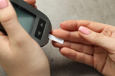 Diabetes. Woman checking blood sugar level with glucometer at gray table, closeup