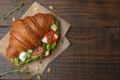 Photo of Tasty croissant with salmon, avocado, mozzarella and lettuce on wooden table, top view. Space for text