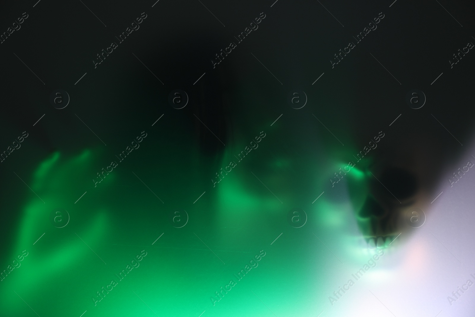 Photo of Silhouette of creepy ghost with skull behind glass against color background