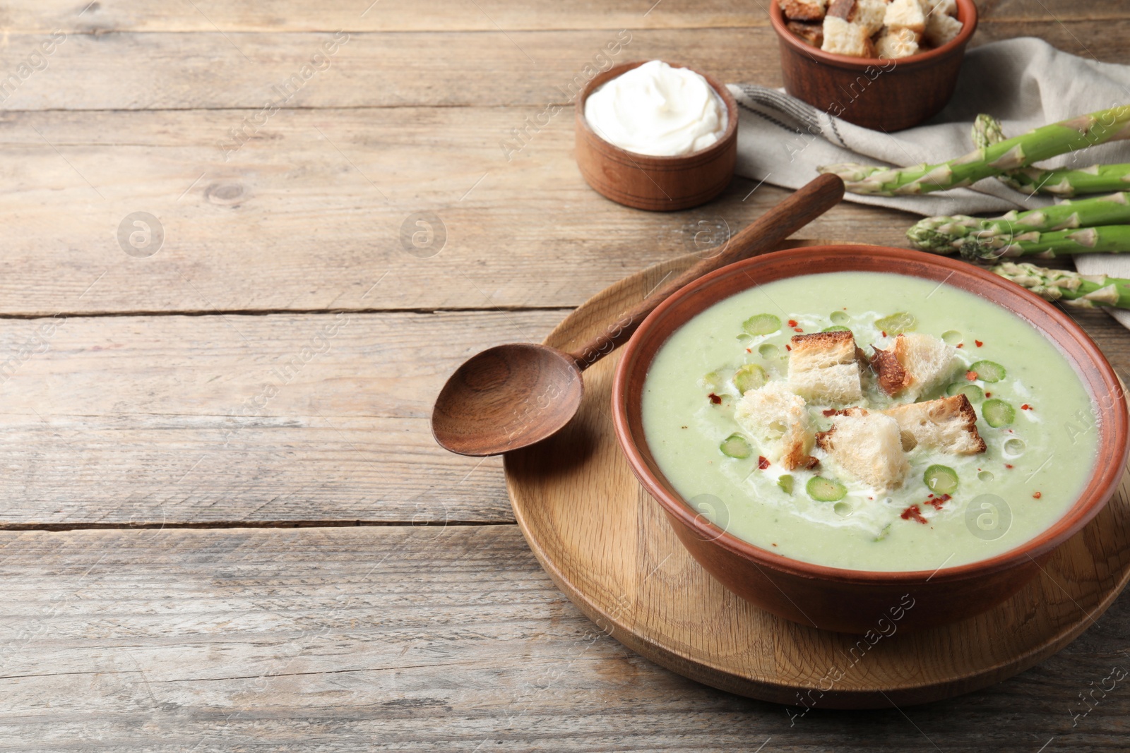 Photo of Delicious asparagus soup with croutons served on wooden table, space for text