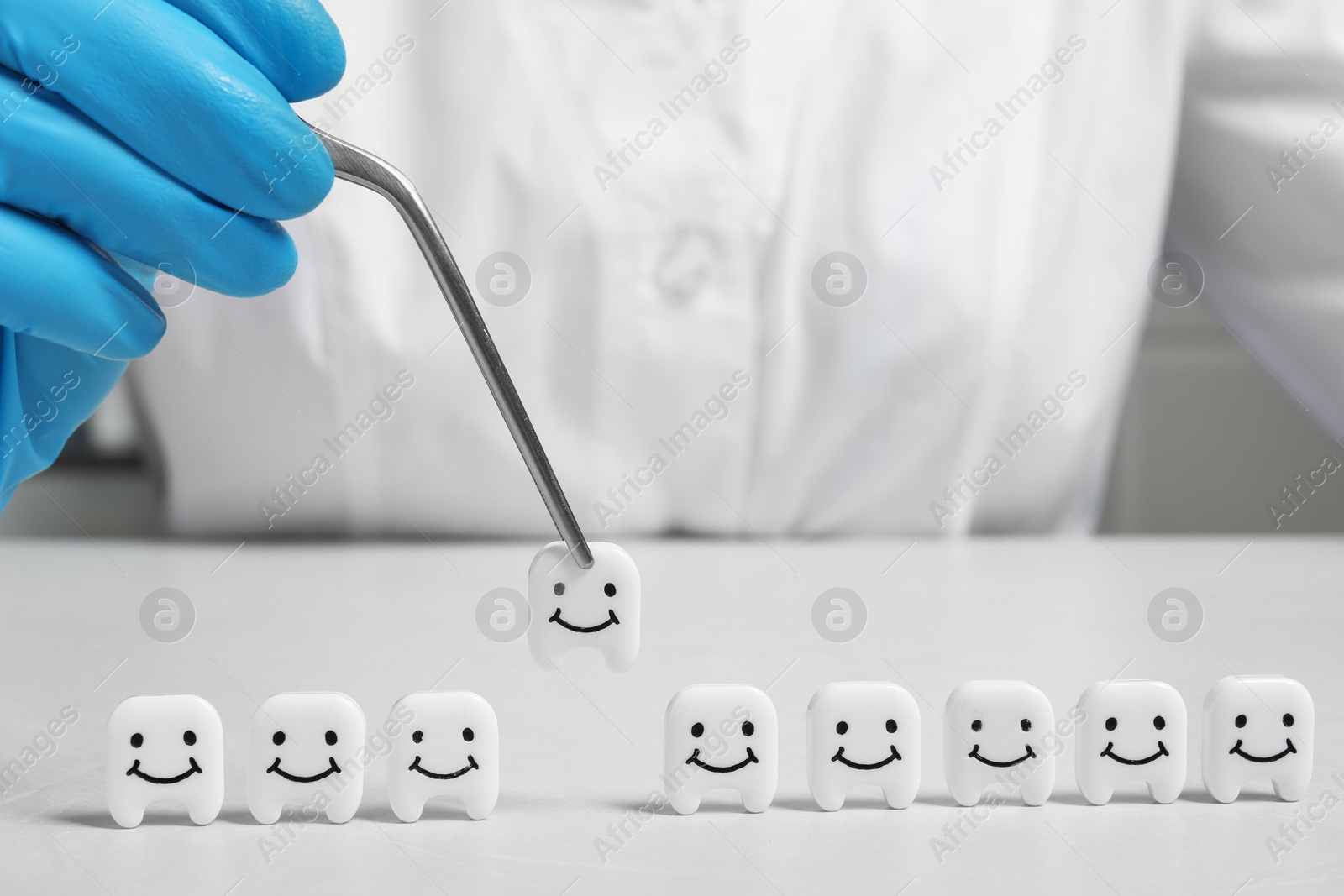 Photo of Dentist with small plastic teeth and tweezers at table
