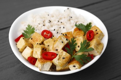 Bowl of rice with fried tofu, chili pepper and parsley on grey wooden table, closeup