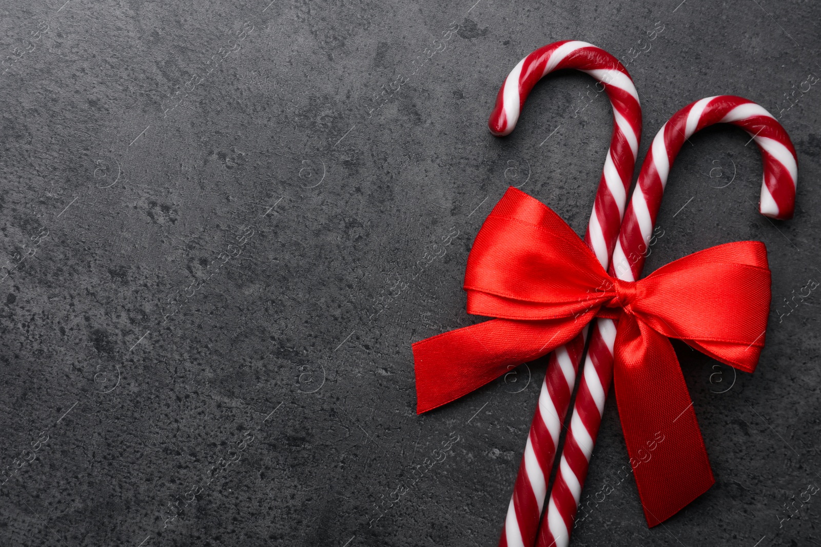 Photo of Sweet Christmas candy canes with red bow on grey background, top view. Space for text