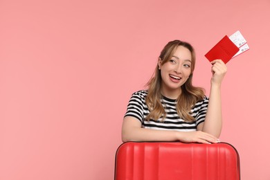 Photo of Happy young woman with passport, ticket and suitcase on pink background, space for text